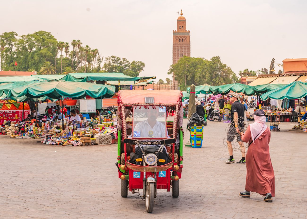 Tuk-tuk driver in Jemaa el-Fna square with market activity in the background
