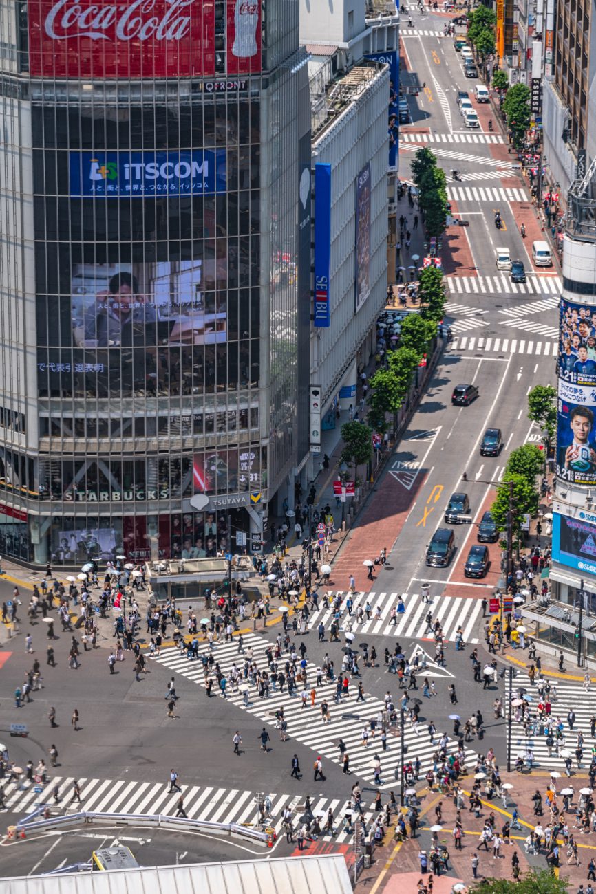 A view of Shibuya Crossing from above, showing the busy intersection and surrounding buildings in central Tokyo.